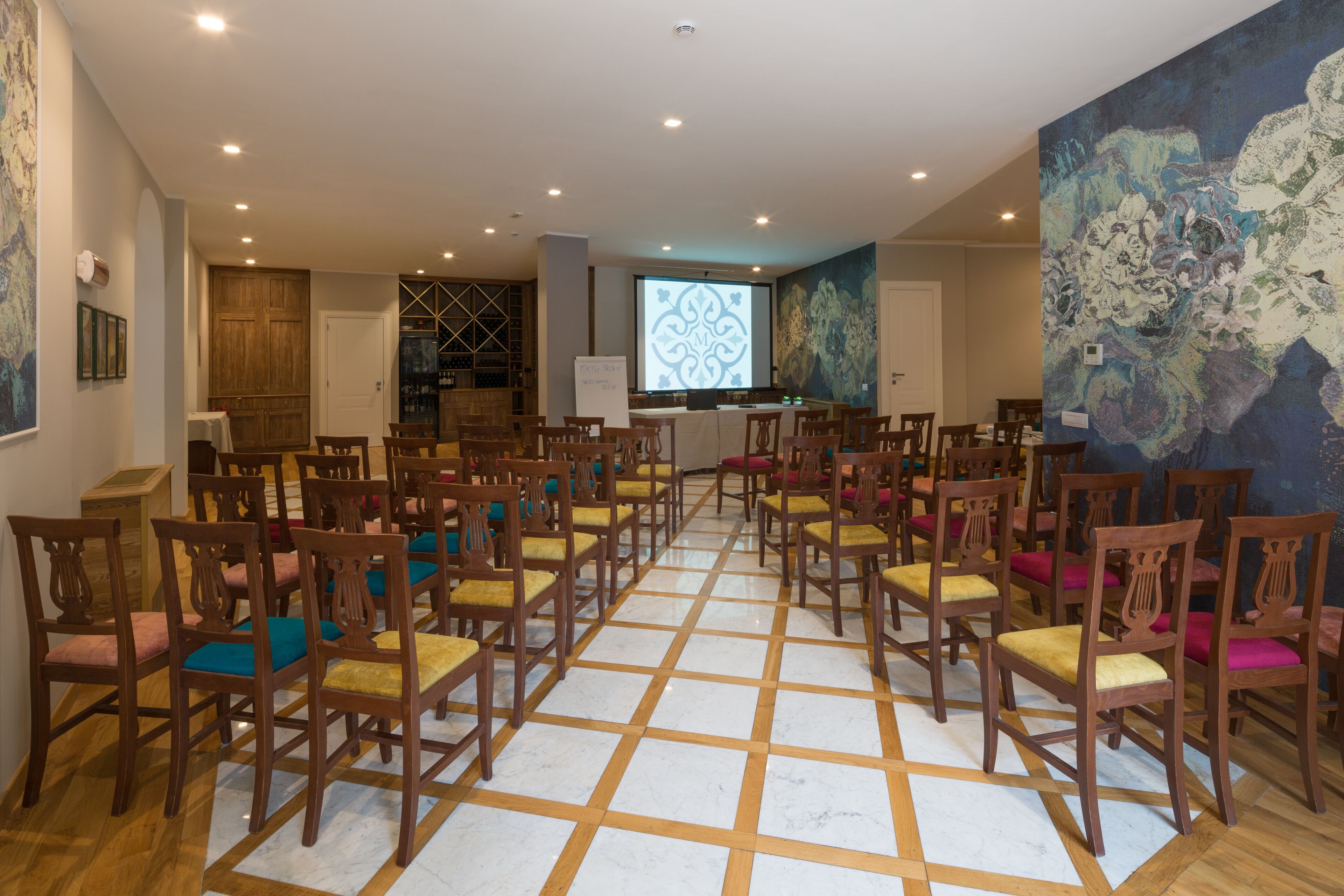 A conference room with wooden chairs arranged in rows, a projector screen, and a large abstract painting on the wall.