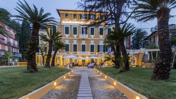 Un hotel con un patio central, palmeras y un camino que lleva a la entrada.