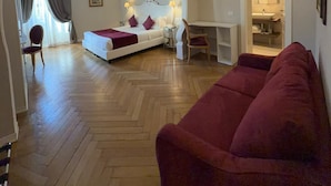 Habitación de hotel con cama, un sofá rojo, un escritorio y un baño visible a través de un arco.