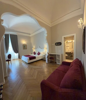 A hotel room with a bed, a red sofa, a desk, and a bathroom visible through an archway.