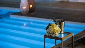 Un área junto a la piscina con un balde de metal y un ramo de flores sobre una mesa de madera.