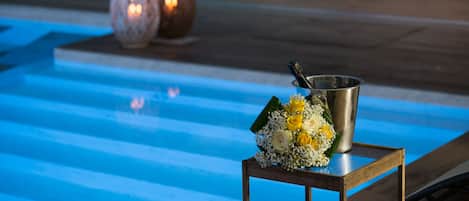 A poolside area with a metal bucket and a bouquet of flowers on a wooden table.