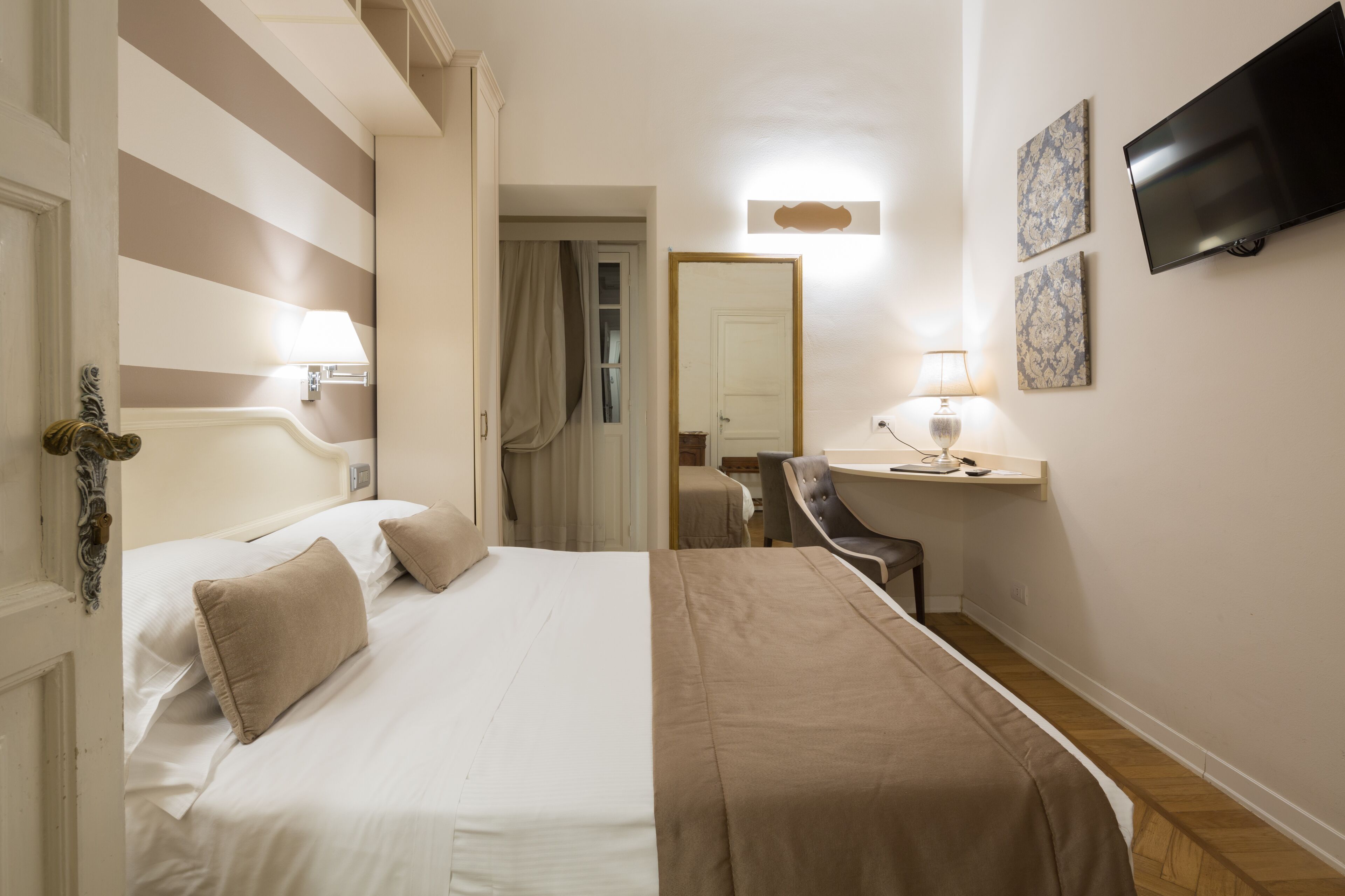 Une chambre d’hôtel équipée d’un lit, d’un bureau, d’une chaise, d’une télévision et d’œuvres d’art accrochées au mur.