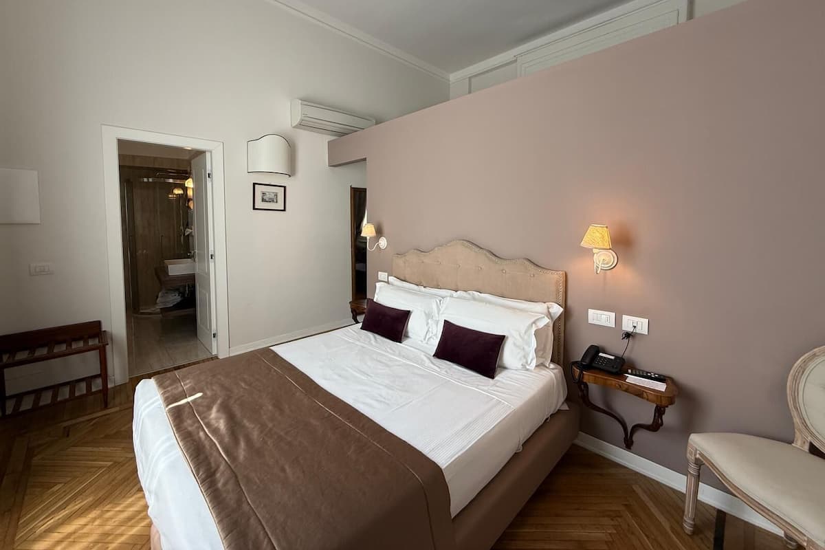 A hotel room with a bed, bedside lamps, a telephone, and a chair.