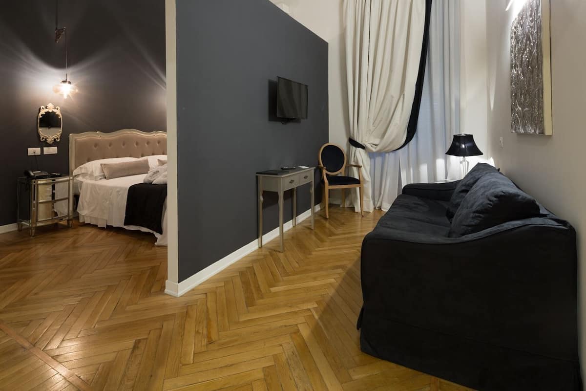A room with a bed, a desk, a chair, a sofa, a TV, and a window with curtains.