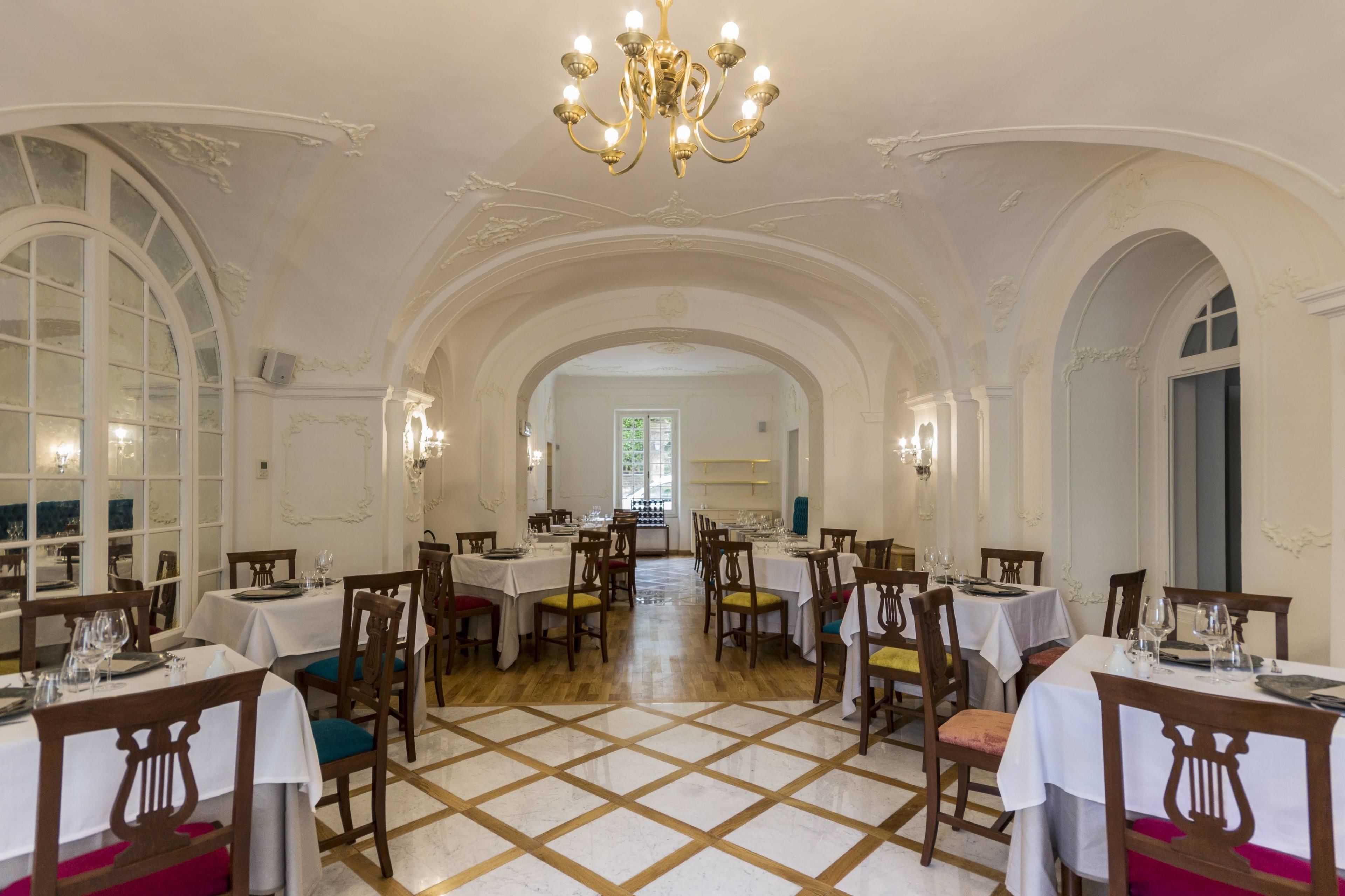 Un comedor con mesas dispuestas para el servicio, una araña y techos abovedados.