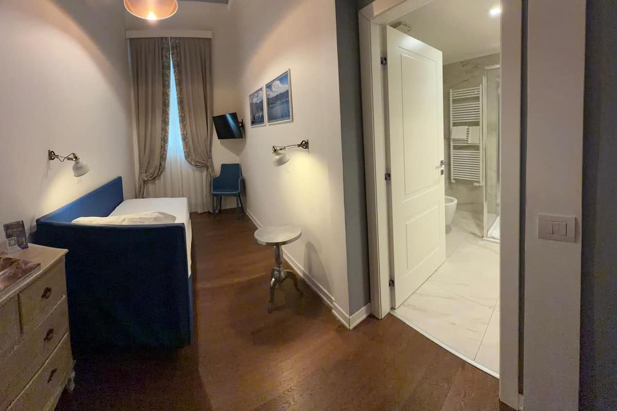 A bedroom with a bed, bedside table, lamp, and a TV on the wall.