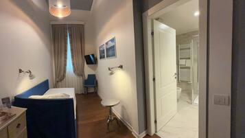 A bedroom with a bed, bedside table, lamp, and a TV on the wall.