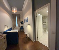 A bedroom with a bed, bedside table, lamp, and a TV on the wall.