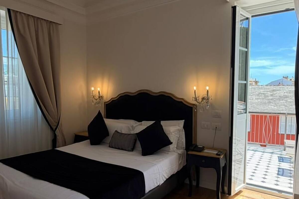 A bedroom with a bed, bedside tables, a chandelier, and a view through an open door.