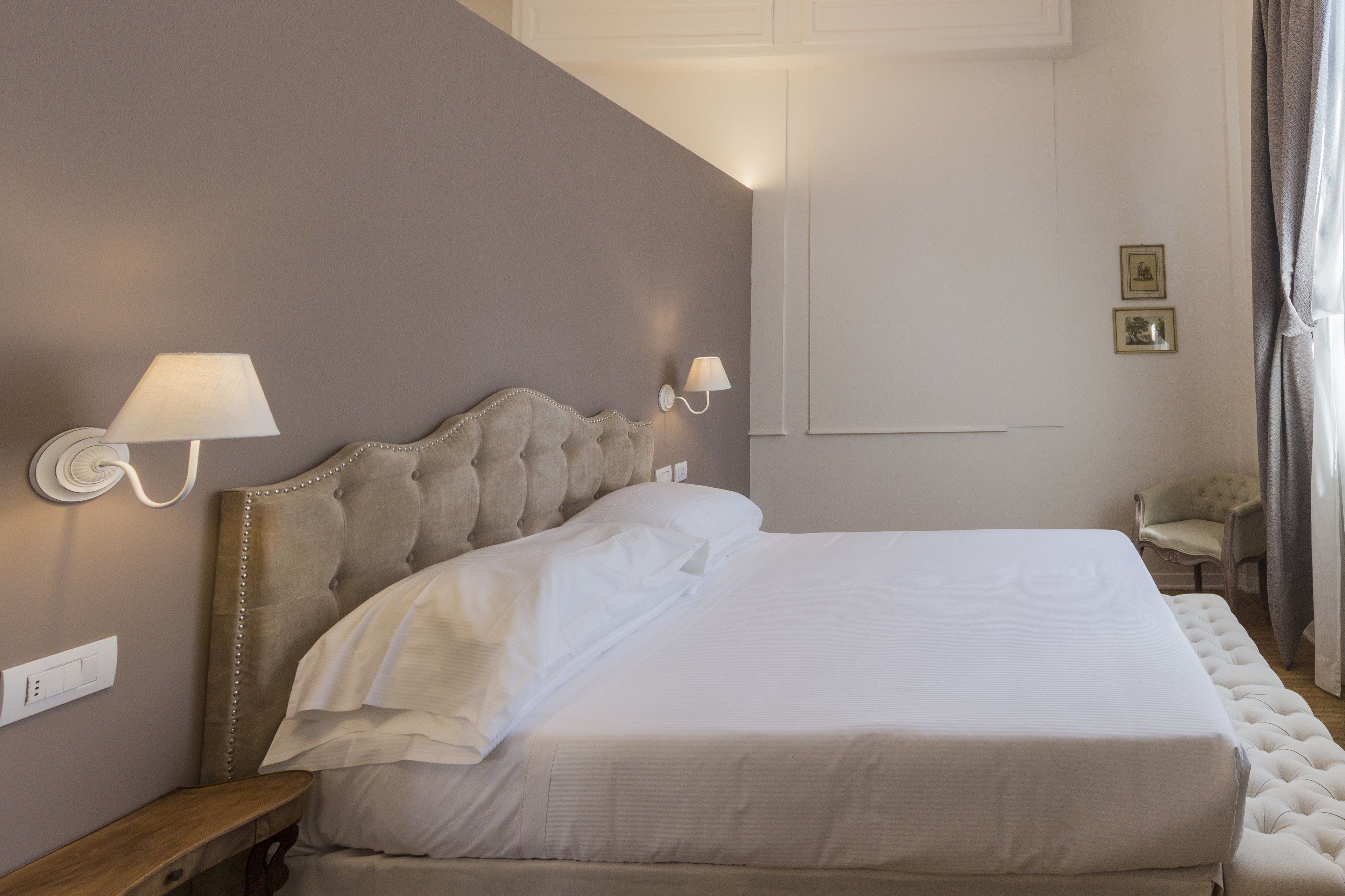 Un letto rifatto con cura, con una testiera imbottita, due lampade ai lati del letto e un piccolo comodino in legno.
