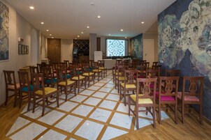 A room with a tiled floor, wooden chairs with cushions, a wooden cabinet, and a wall with a large painting.