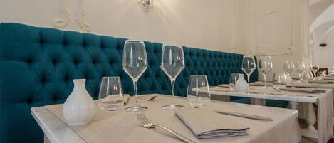 Un área de comedor con asientos tapizados en color aguamarina, vajilla blanca y una lámpara fijada a la pared.