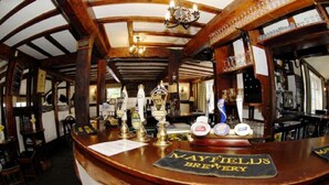 A bar area with a wooden counter, a sign reading "Mayfield's Brewery," and various bottles and glasses. - England's Gate and Coachhouse (Hereford)