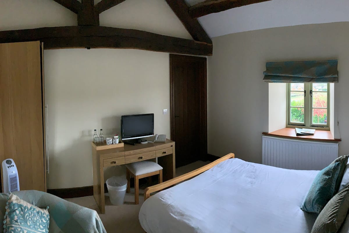 A bedroom with a bed, a desk with a computer, a window, and a radiator.