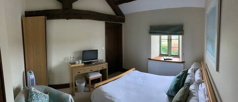 A bedroom with a bed, a desk with a computer, a window, and a radiator.