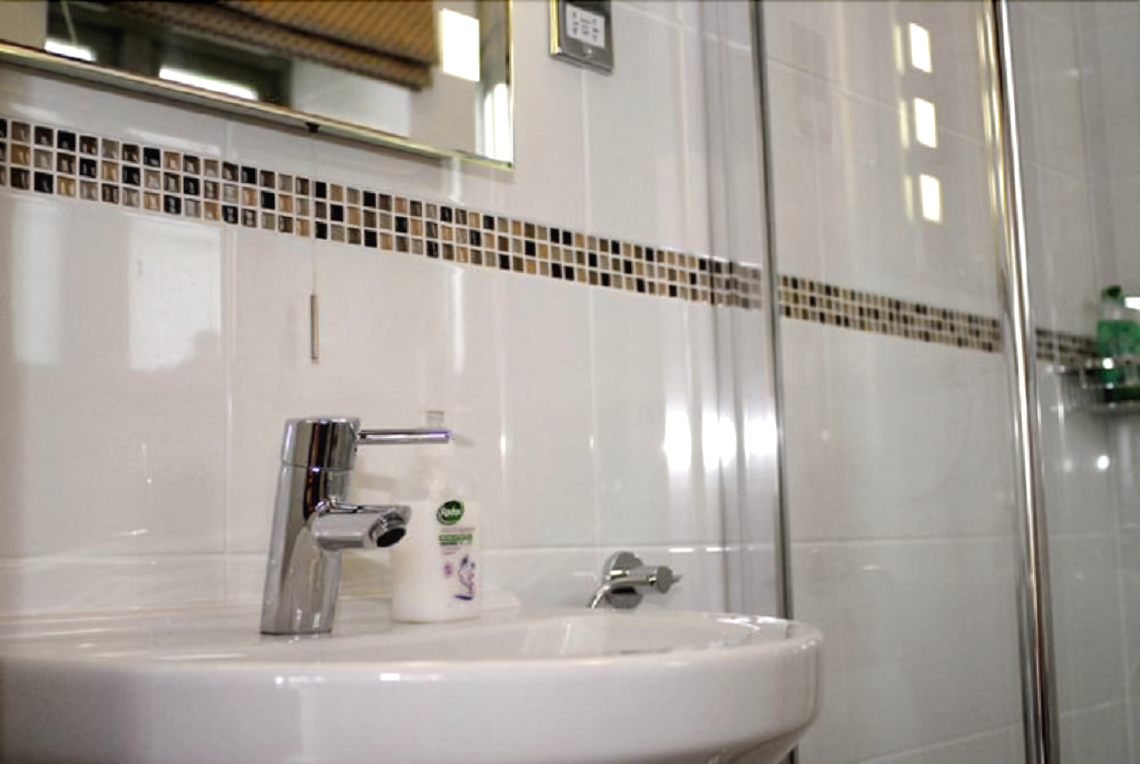 Un baño con lavamanos blanco, grifo de cromo y un espejo encima.