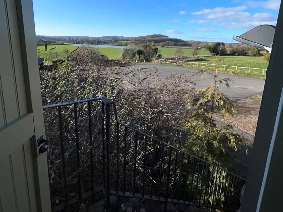 A view from a window overlooking a rural landscape with fields, a body of water, and distant hills.