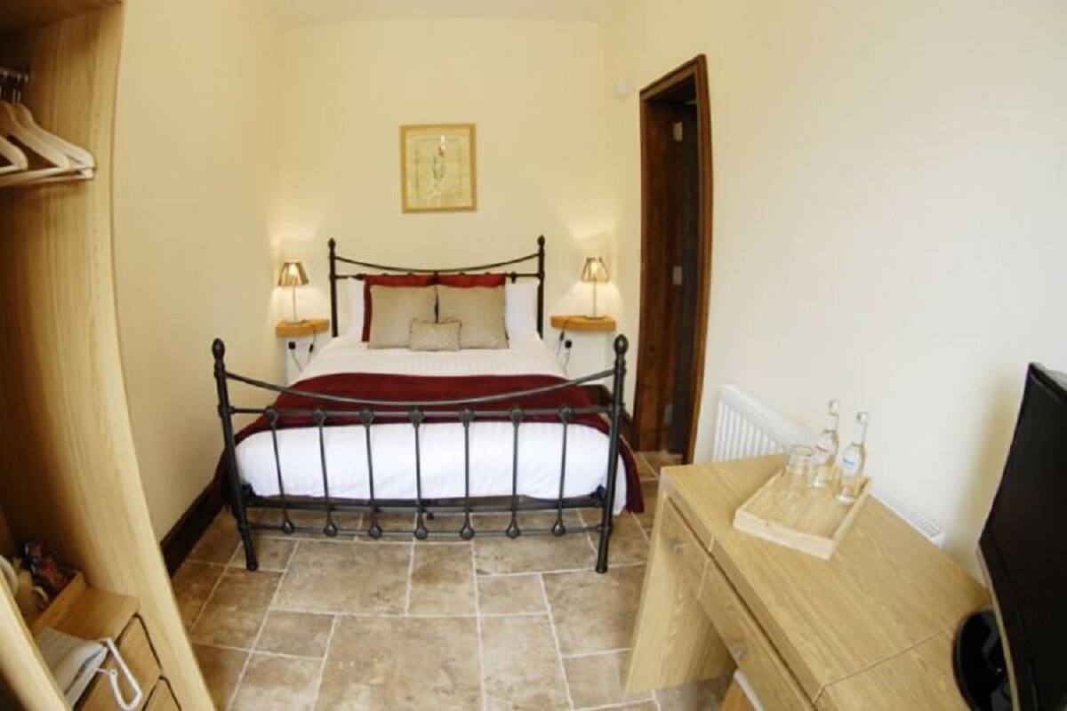 A bedroom with a metal bed frame, white bedding, two bedside lamps, a wooden dresser, and a radiator.