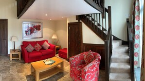 A living room with a red sofa, a coffee table, a TV, and a staircase. - England's Gate and Coachhouse (Hereford)