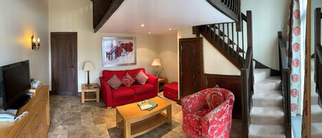 Una sala de estar con un sofá rojo, una mesa de centro, un televisor y una escalera.