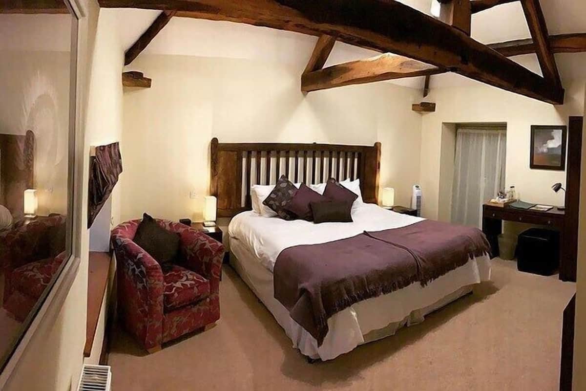 A bedroom with a large bed, a wooden headboard, a red armchair, and a bedside table with a lamp.
