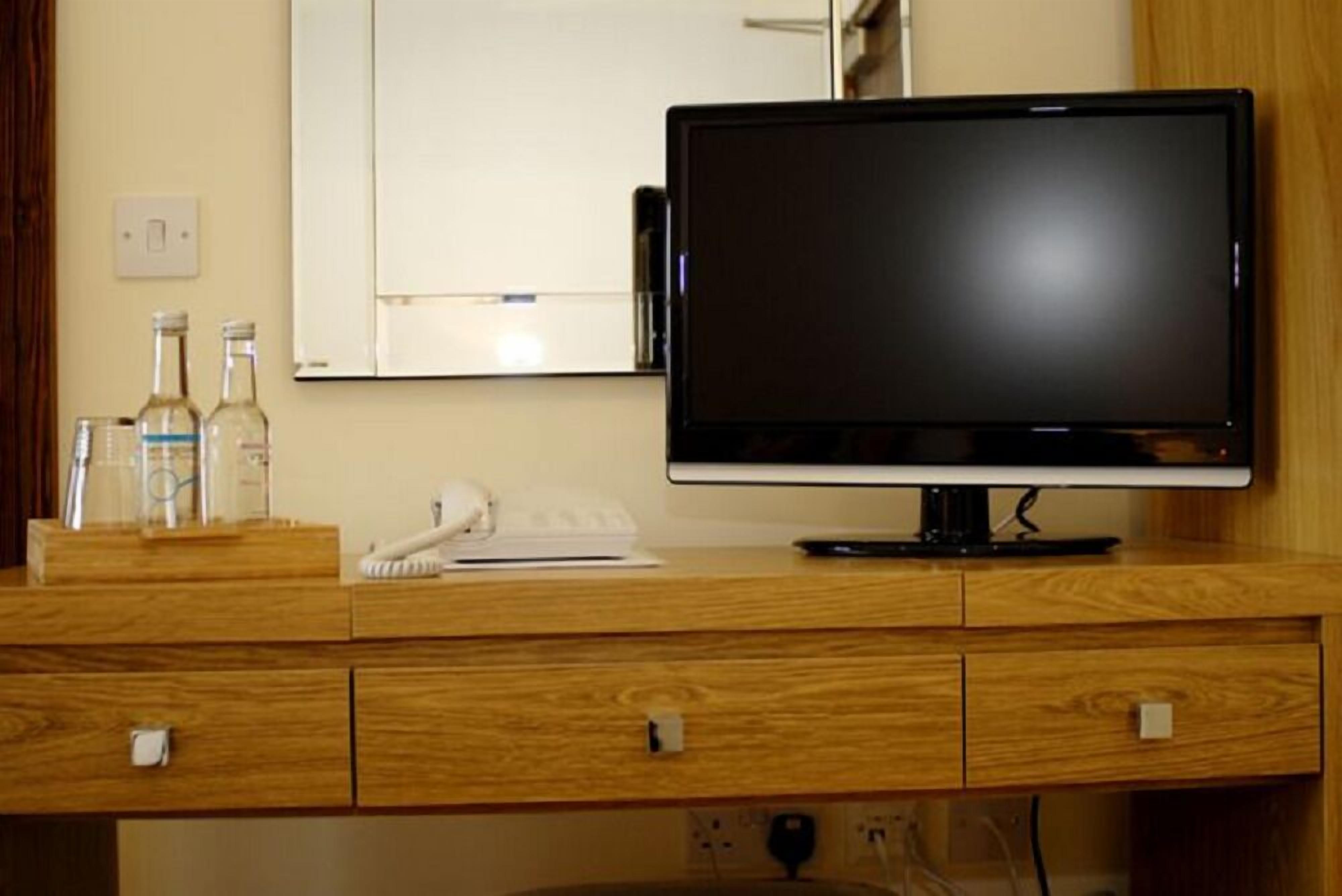 Un escritorio de madera con un monitor de pantalla plana, un teléfono y algunas botellas.