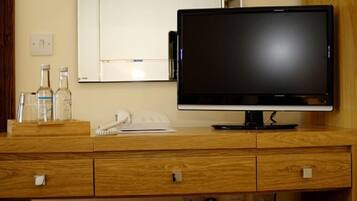 Un escritorio de madera con un monitor de pantalla plana, un teléfono y algunas botellas.