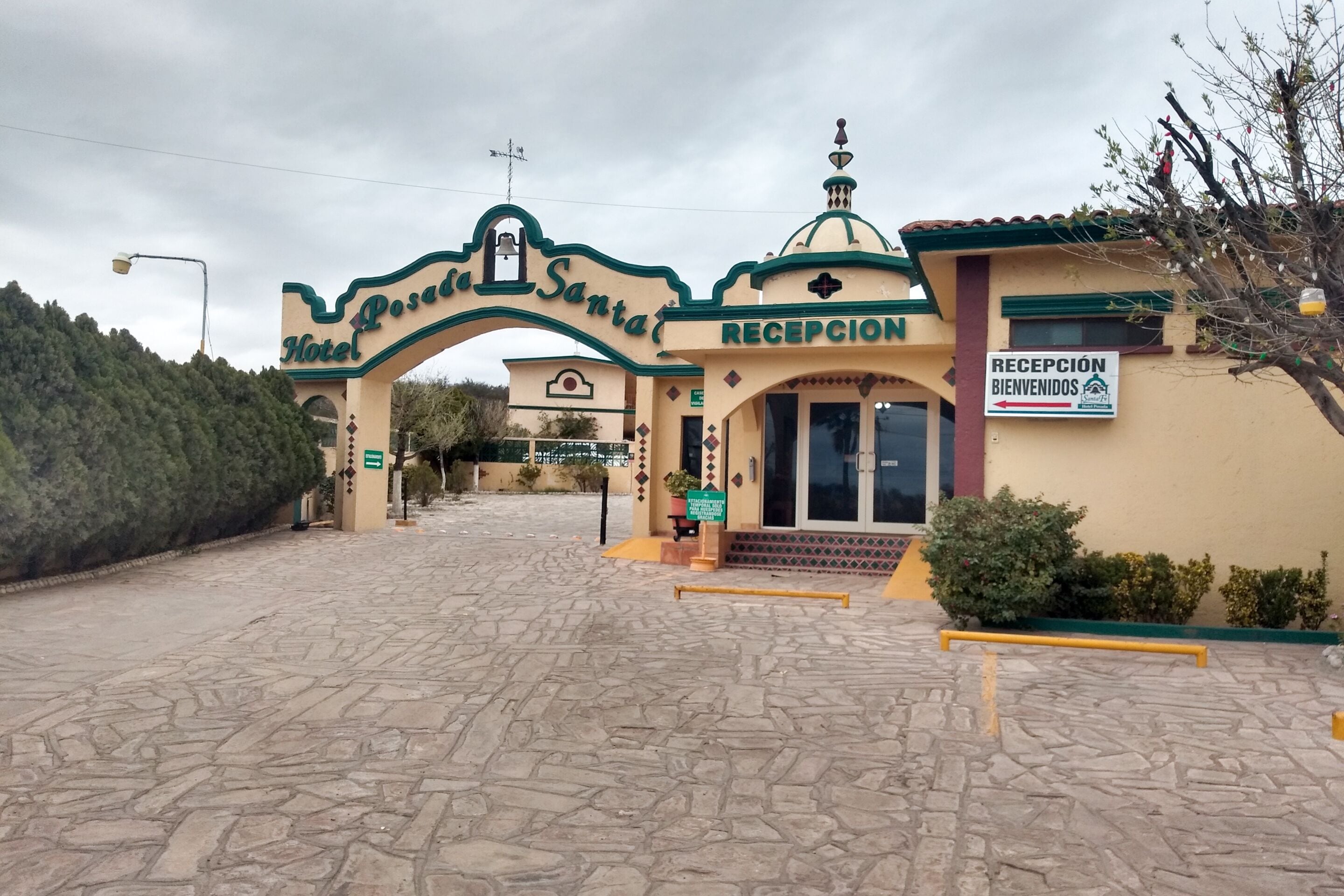 Entrada de hotel con recepción, una torre de campanas y un letrero dando la bienvenida a los huéspedes.