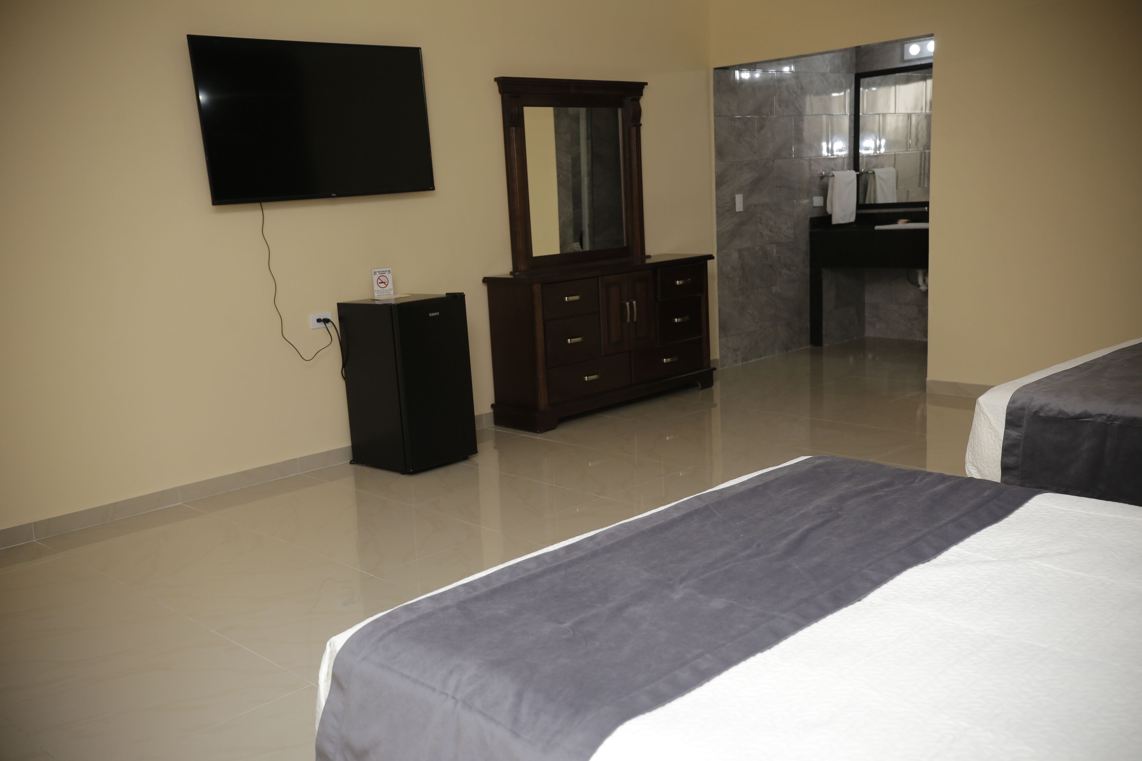A hotel room with a bed, a TV mounted on the wall, a dresser, and a bathroom visible through an open door.