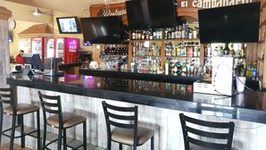 A bar area with a counter, bar stools, a television mounted above the counter, and shelves stocked with various bottles. - Hotel Posada Santa Fe Sabinas (Sabinas)