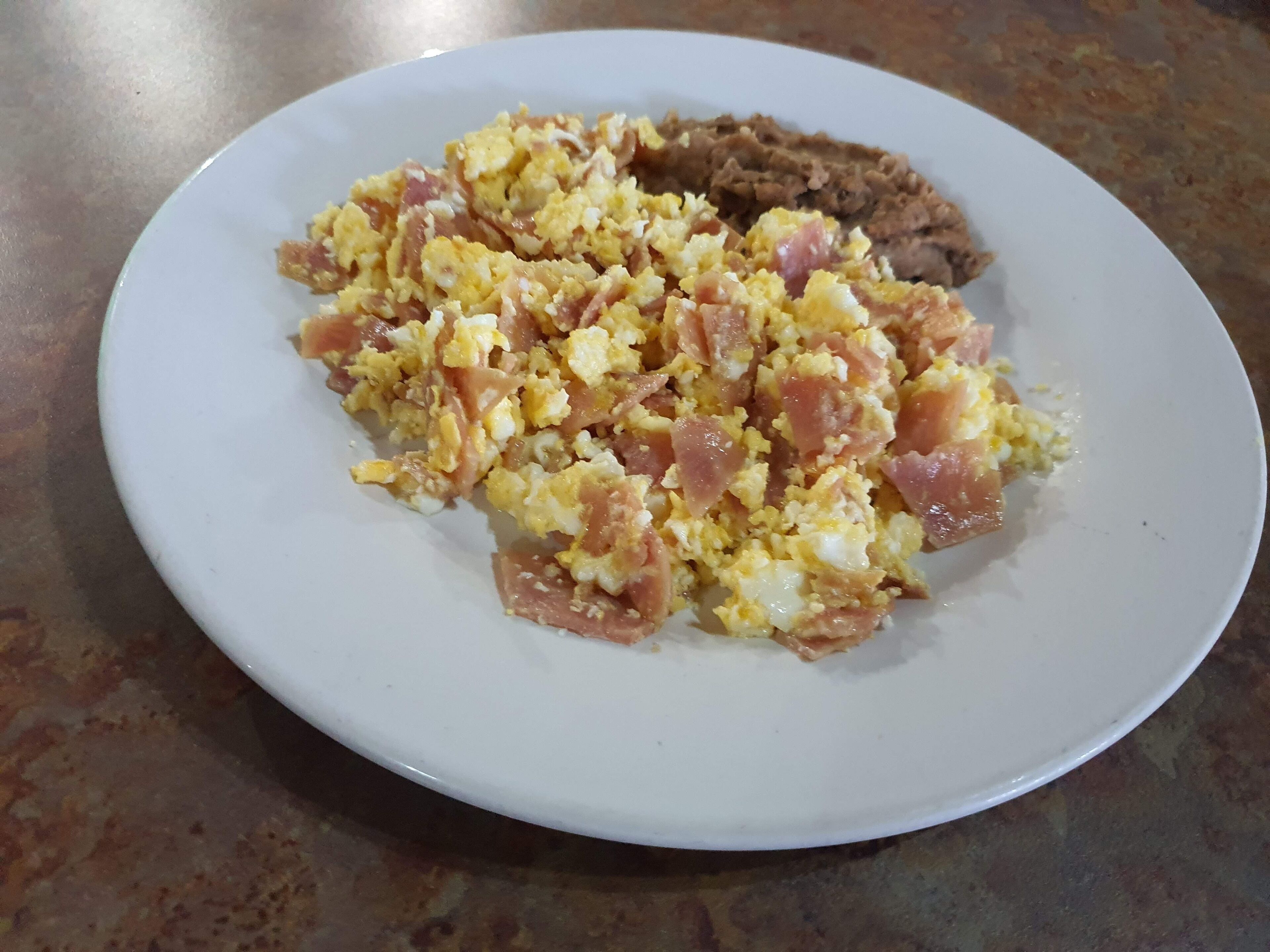 Une assiette blanche contenant des œufs brouillés et des haricots.