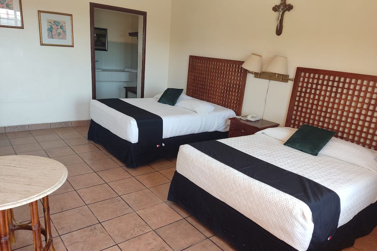 Una habitación de hotel con dos camas, cabecero de madera, una mesita y un espejo.