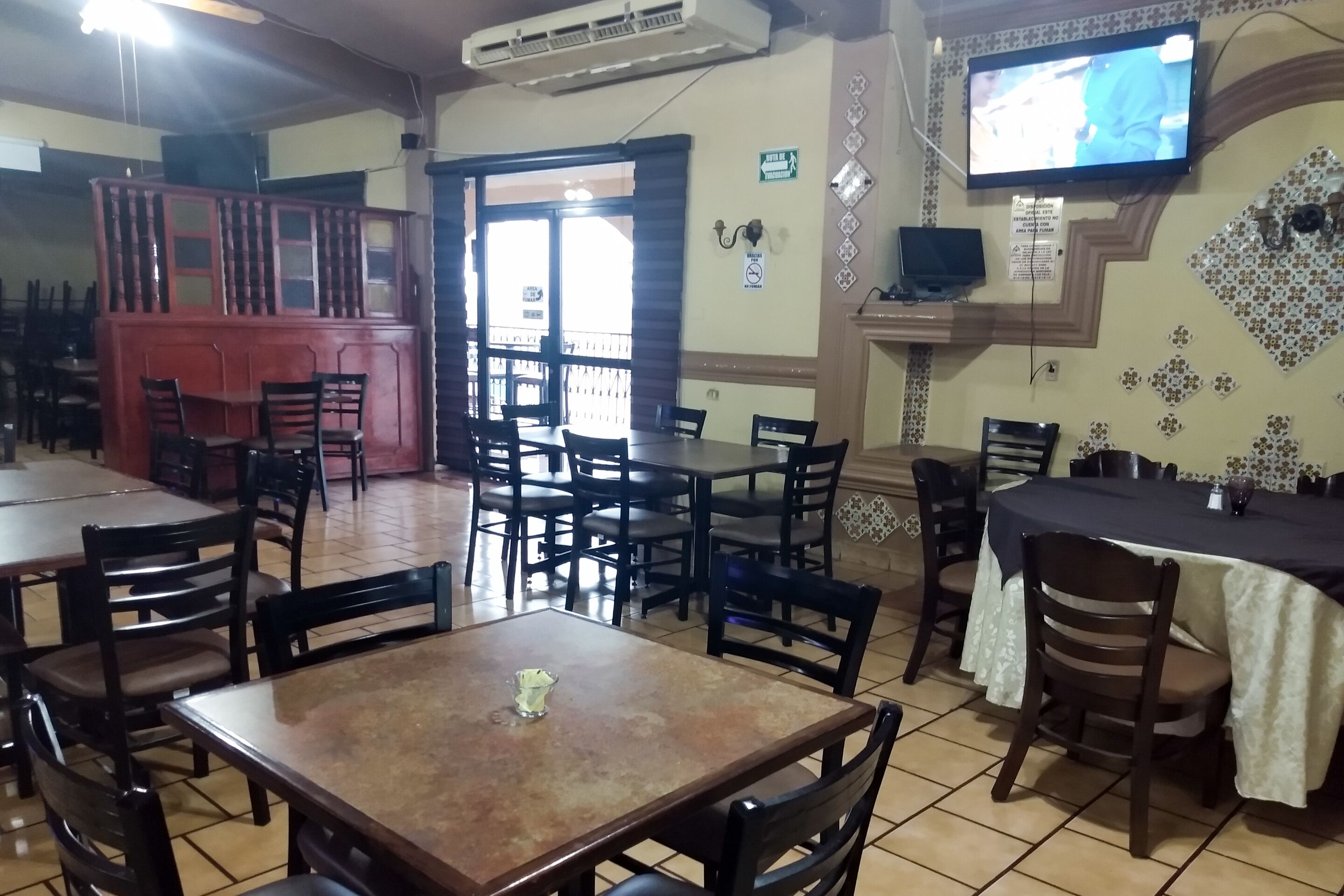 A restaurant with multiple tables and chairs, a television mounted on the wall, and a decorative wall pattern.