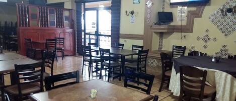 A restaurant with multiple tables and chairs, a television mounted on the wall, and a decorative wall pattern.