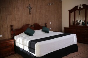 Un dormitorio con cabecera de madera, una cama grande con ropa de cama blanca, dos almohadas verdes, un aparador de madera y un espejo con marco de madera.