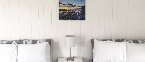 Una habitación de hotel con dos camas, una mesita de noche con lámpara y un cuadro con un paisaje al atardecer.
