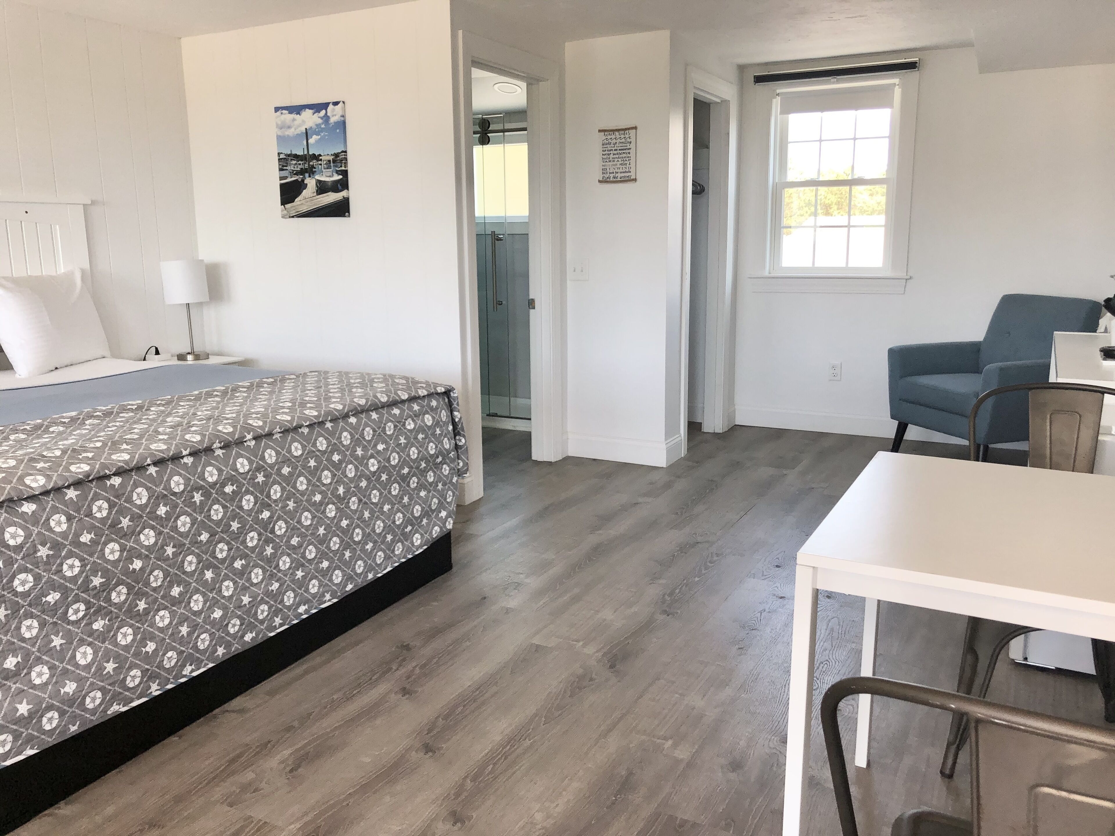 Een kamer met een bed, een bureau, een stoel, een raam en een deur die naar een andere kamer leidt.