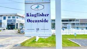 En skylt för Kingfisher Oceanside med en fågel som logotyp, placerad på en parkeringsplats med byggnader i bakgrunden.