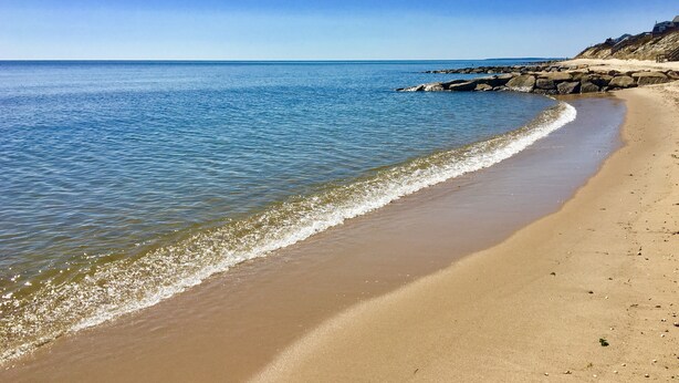 En strand med kristallklart blått vatten, en sandstrand och klippiga utskjutande partier.