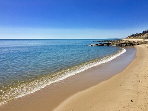 Ein Strand mit klarem, blauem Wasser, einem Sandufer und Felsformationen.