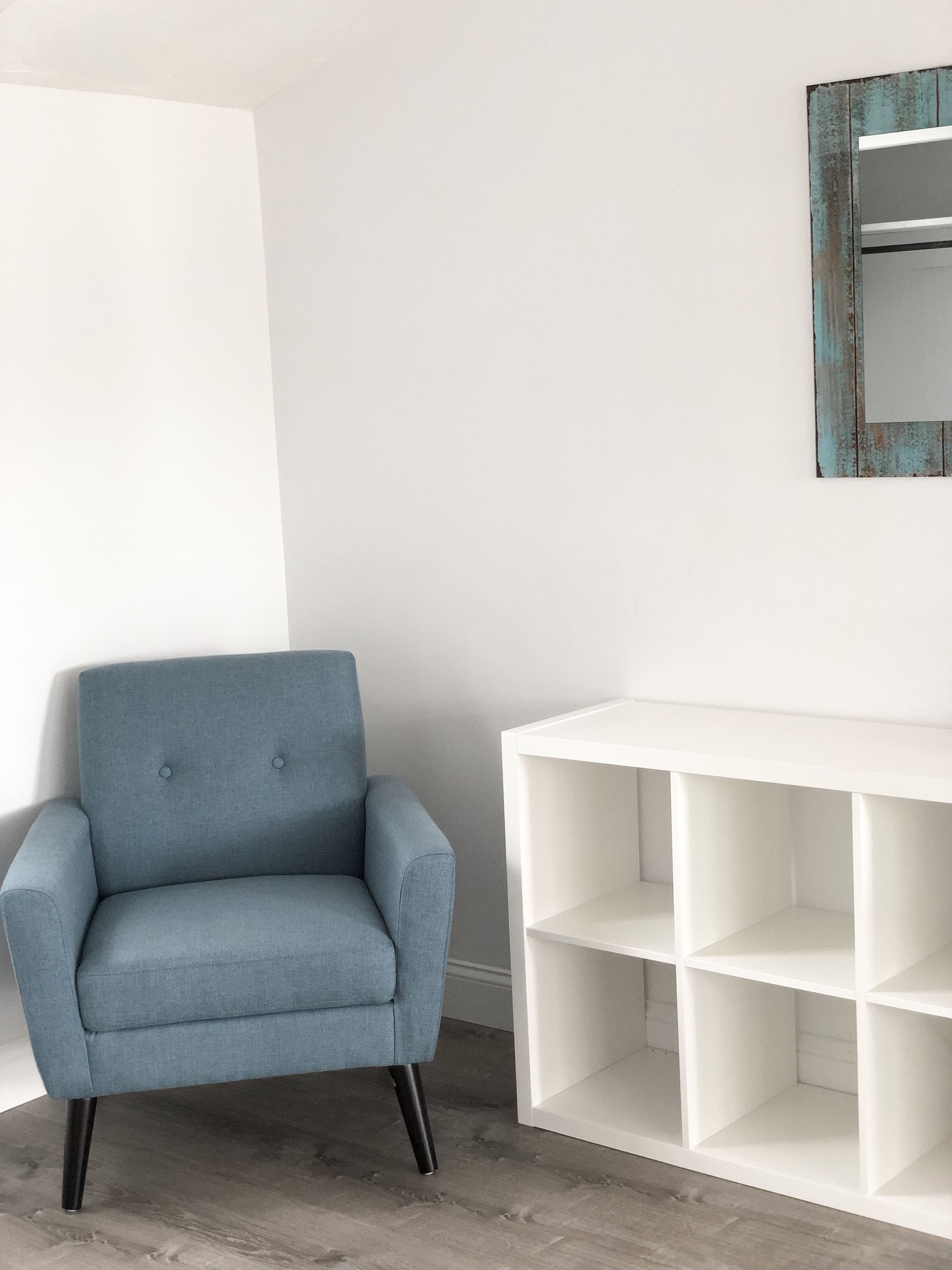 A room with a blue armchair, a white console table, and a mirror with a rustic frame.