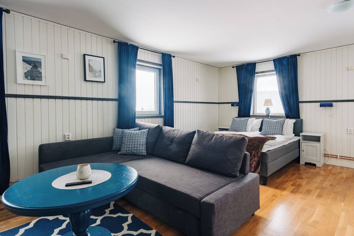 A modern room with a grey sofa, a small round table, and a bed with a white headboard.