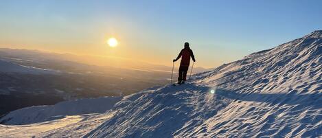 Una persona esquiando por una pendiente nevada bajo un cielo despejado, con el sol poniéndose en el horizonte.