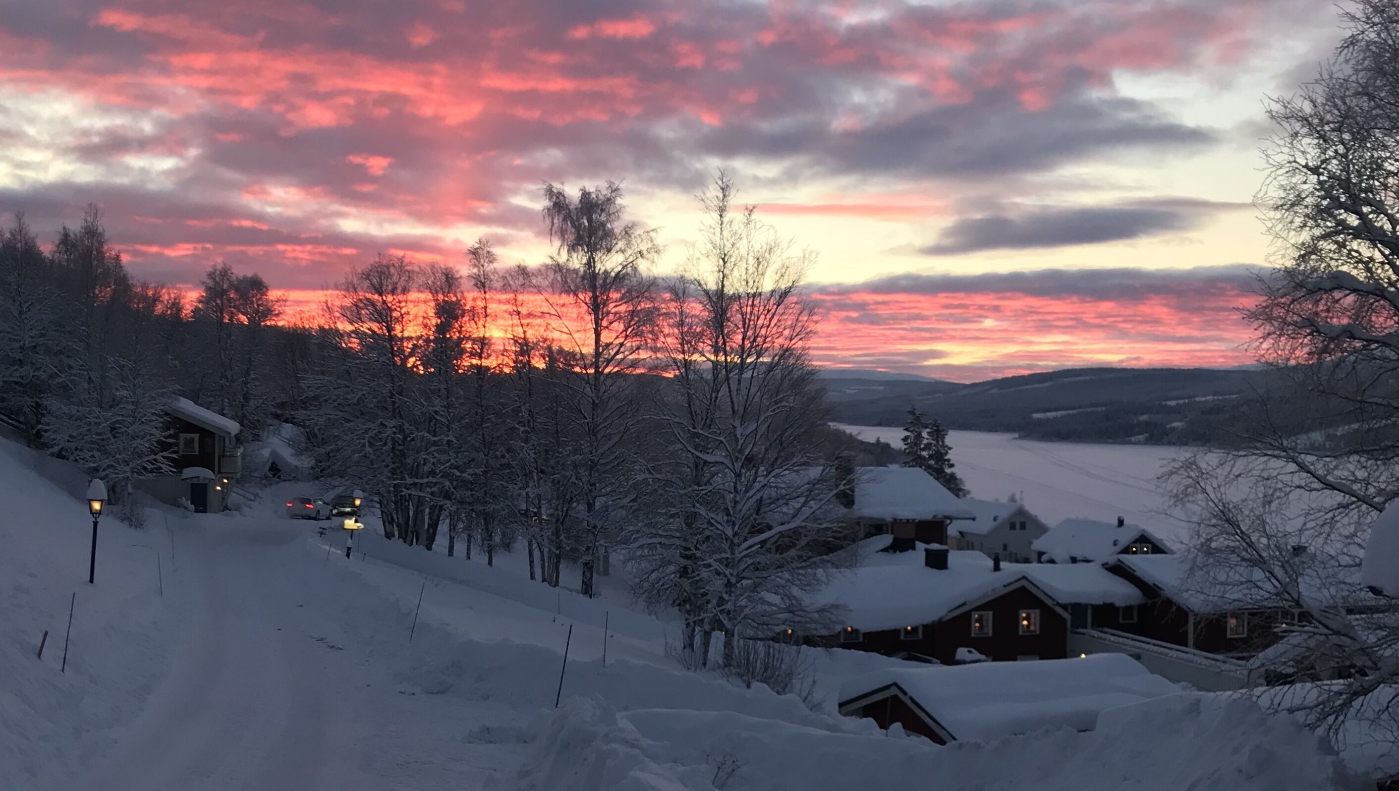 A snowy landscape with houses and a sunset.