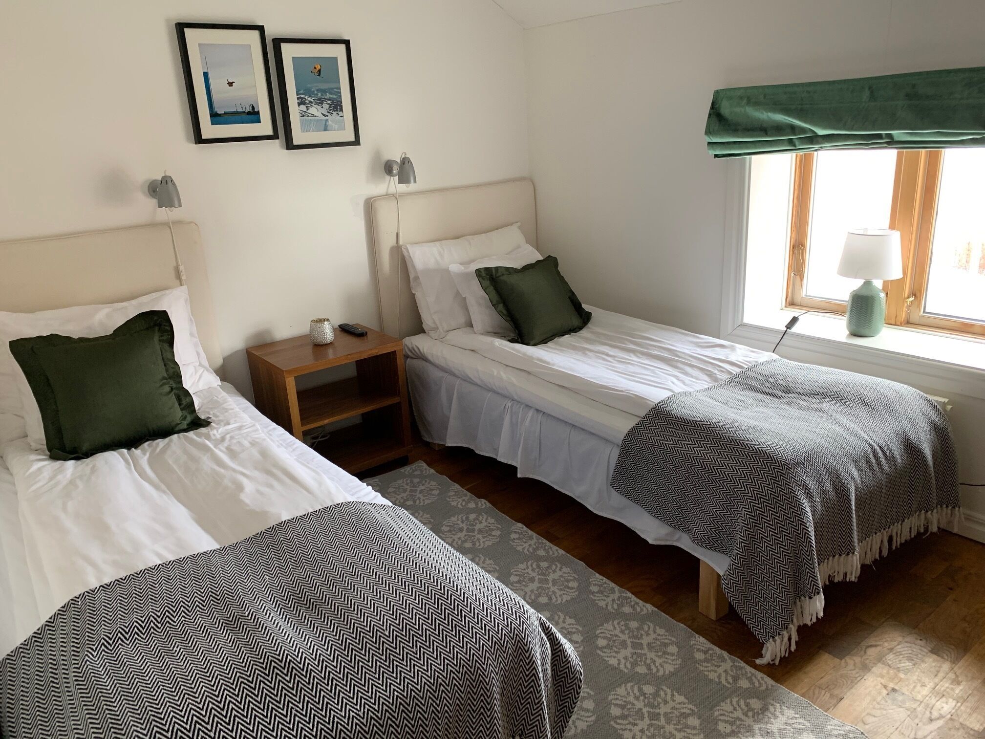 Une chambre avec deux lits simples, une table de chevet, une lampe et une fenêtre donnant sur un beau paysage.