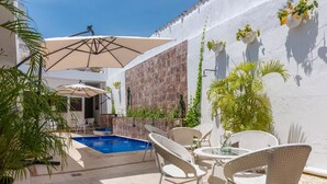 A pool area with white wicker furniture and umbrellas, surrounded by white walls and plants. - Casa Arte Hotel Boutique by HMC - Adults Only (Cartagena)