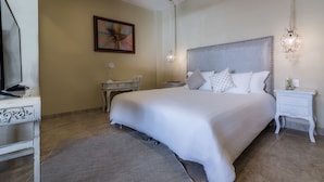 A neatly arranged bedroom with a large bed, a bedside table, a nightstand, a television, and a decorative wall piece. - Casa Arte Hotel Boutique by HMC - Adults Only (Cartagena)