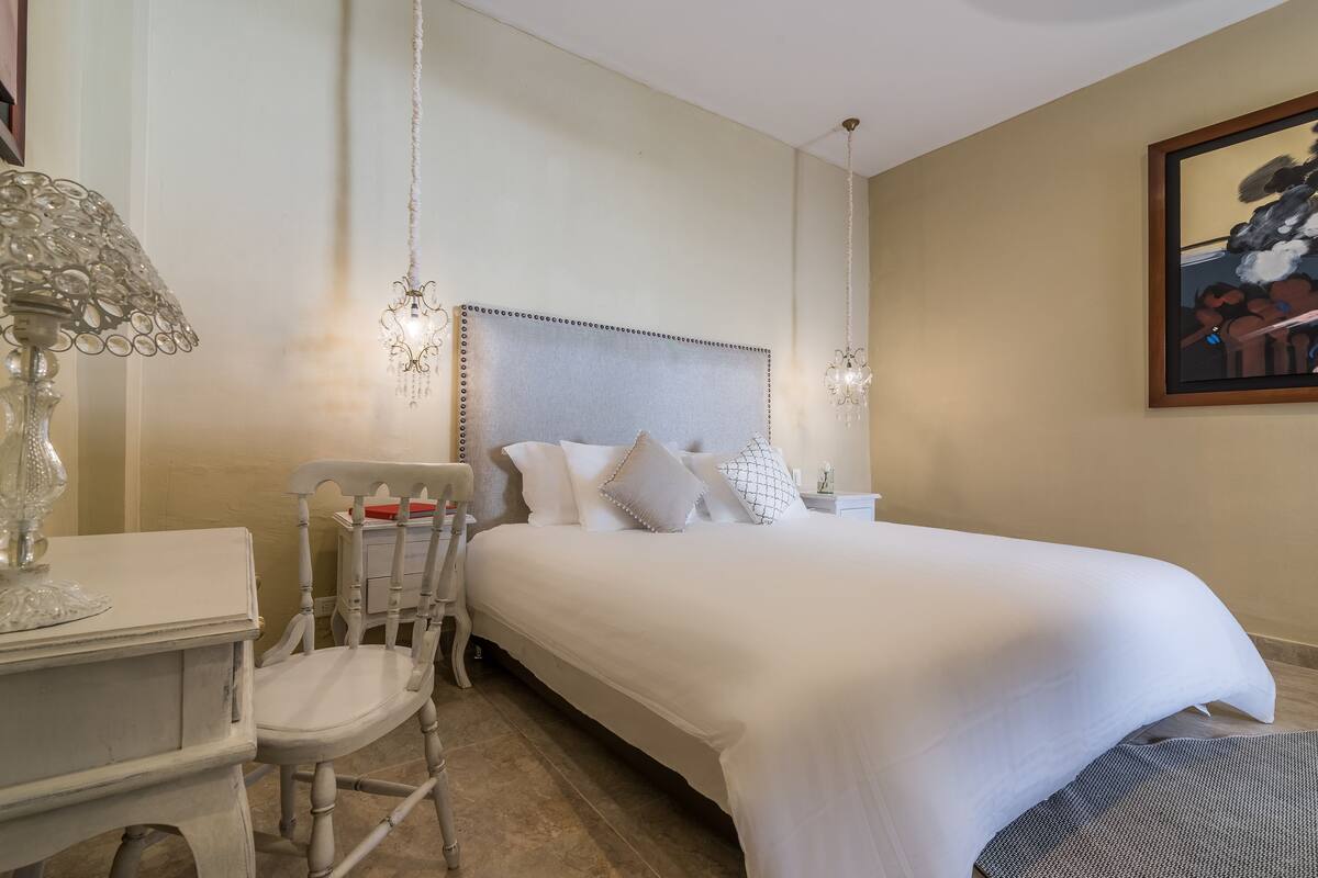 A neatly arranged bedroom with a large bed, a chair, a small table, and a chandelier.