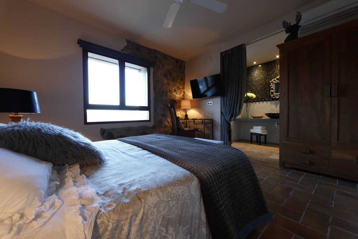 A bedroom with a bed, a television, a wardrobe, and a stone wall.